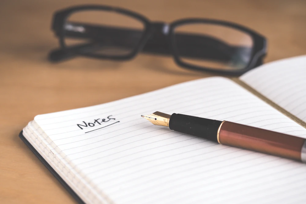 A handwritten checklist in a notebook beside a pen